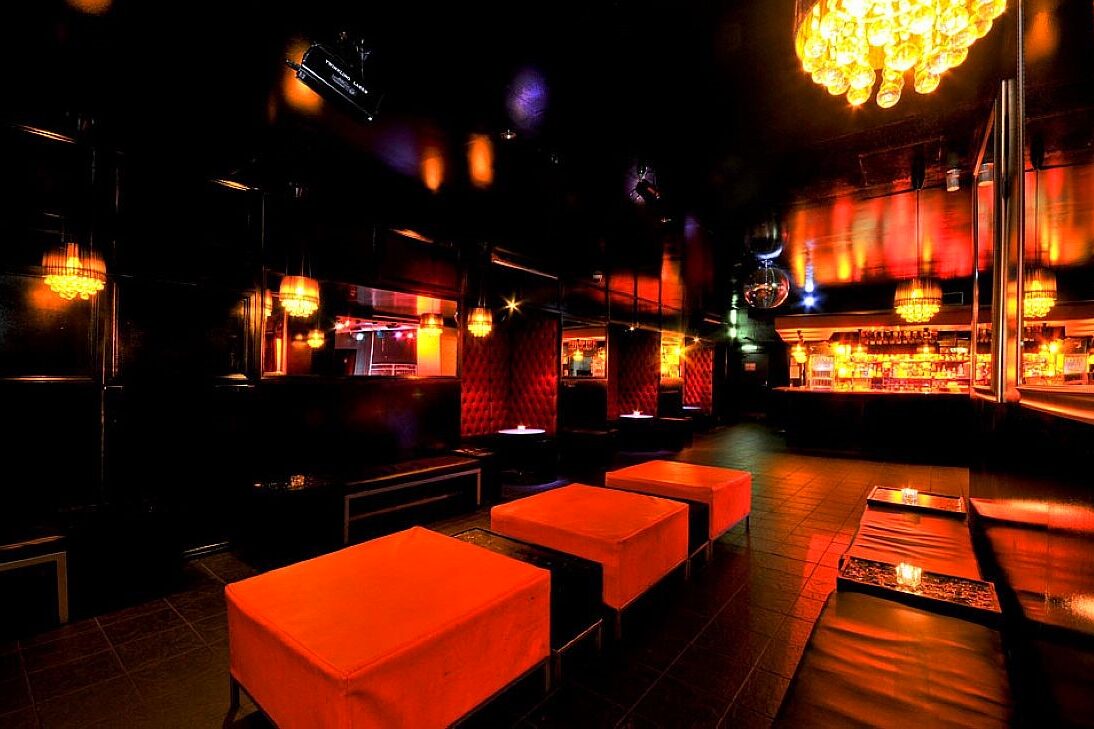 The Basement lounge in warm amber light, with orange ottomans and banquette seating leading back towards the bar and mirror ball
