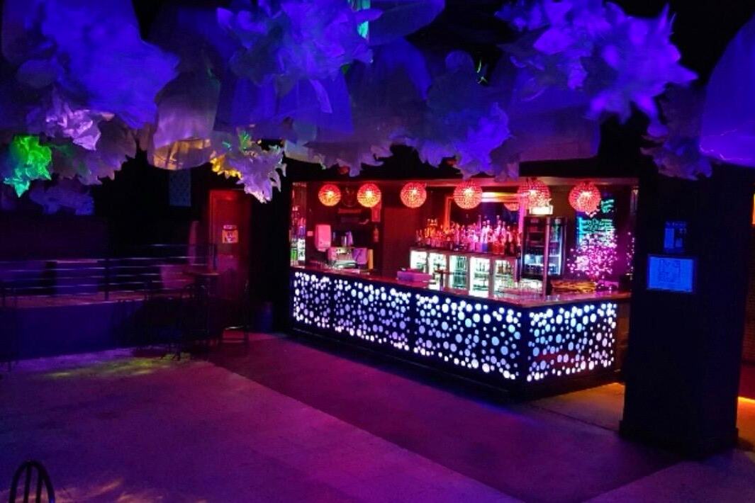 The Café bar counter, backlit and hung with red paper lanterns, beneath a sculpted ceiling washed in purple light
