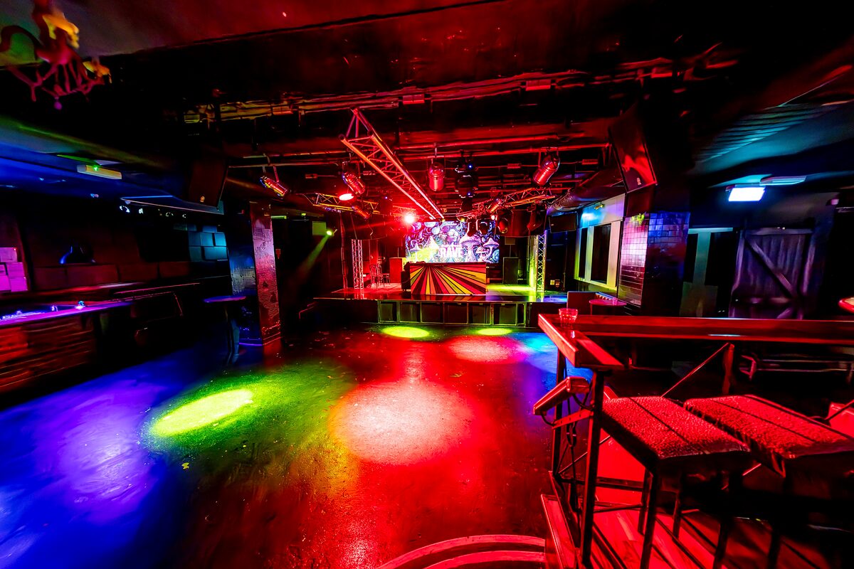The Main Room dance floor lit in red, green and blue, looking towards the stage and screen with the overhead lighting rig and raised bar seating to one side